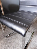 Mid-Century Modern bistro table with speckled granite top and chrome base, flanked by two black ribbed faux leather cantilever chairs on a grey carpet.