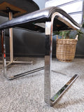 Mid-Century Modern bistro table with speckled granite top and chrome base, flanked by two black ribbed faux leather cantilever chairs on a grey carpet.