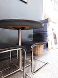 Mid-Century Modern bistro table with speckled granite top and chrome base, flanked by two black ribbed faux leather cantilever chairs on a grey carpet.