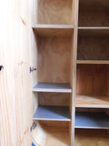 Full view of a tall, artisan-crafted wardrobe from the early 2000s. It features a bold geometric pattern of red, black, and natural birch plywood triangles on its doors, framed by polished metal rounded edges. An open cubby is visible in the center. The base is also metal-clad with cut-out shapes.