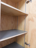 Full view of a tall, artisan-crafted wardrobe from the early 2000s. It features a bold geometric pattern of red, black, and natural birch plywood triangles on its doors, framed by polished metal rounded edges. An open cubby is visible in the center. The base is also metal-clad with cut-out shapes.