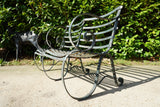 Antique Victorian slatted wrought iron garden bench with scrolled arms in weathered green paint set against a hedge