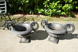 Pair of vintage black cast iron campana garden urn planters with scroll handles and flower medallions on concrete backdrop