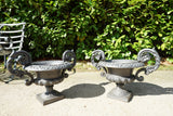 Pair of vintage black cast iron campana garden urn planters with scroll handles and flower medallions on concrete backdrop