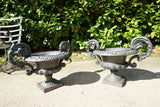 Pair of vintage black cast iron campana garden urn planters with scroll handles and flower medallions on concrete backdrop